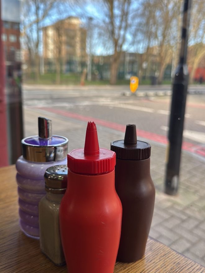 Ketchup, brown sauce and condiment shakers on a table by the window
